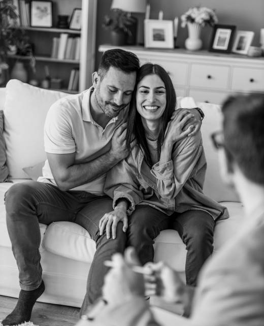 Happy couple embracing on a sofa during a therapy session, with a psychologist attentively taking notes and fostering open communication